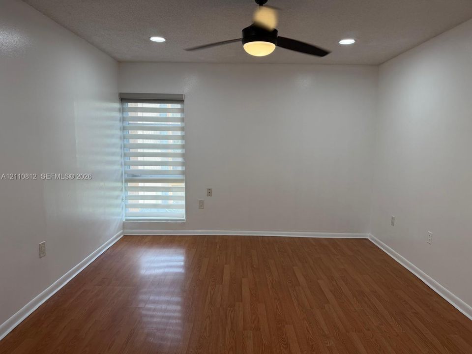 Interior space featuring wood-finish flooring, a neutral color palette, recessed lighting, a modern ceiling fan with integrated lighting, and a window with a dual-layer roller shade