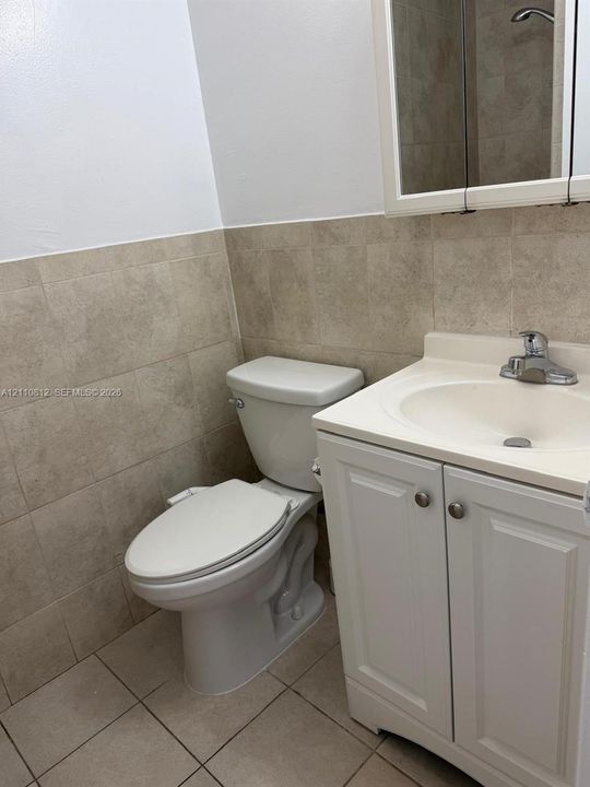 White vanity with integrated basin and polished metal faucet, complemented by neutral-toned wall and floor tiling, and a recessed medicine cabinet