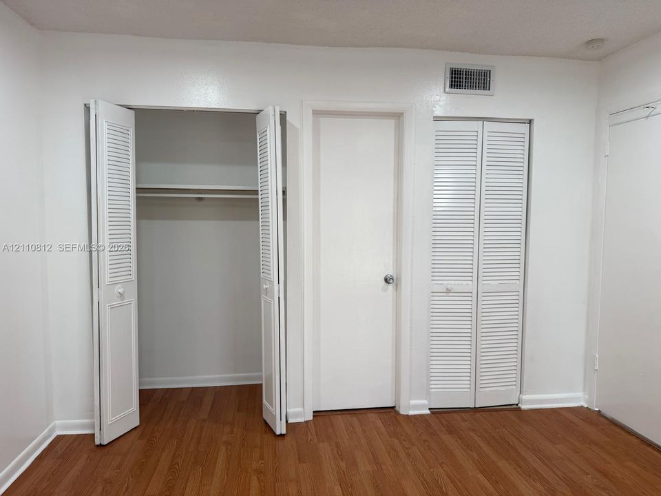 Wood-finish flooring, dual closets with white louvered doors, and a centered solid-core door