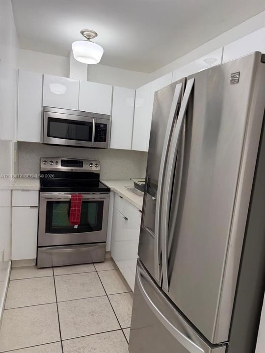 Kitchen featuring gloss-finish white cabinetry, stainless steel appliances, solid-surface countertops, and tile flooring