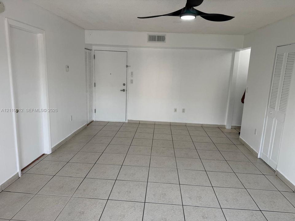 Neutral-toned tile flooring, three-blade ceiling fan with integrated light fixture, and multiple louvered-style closet doors