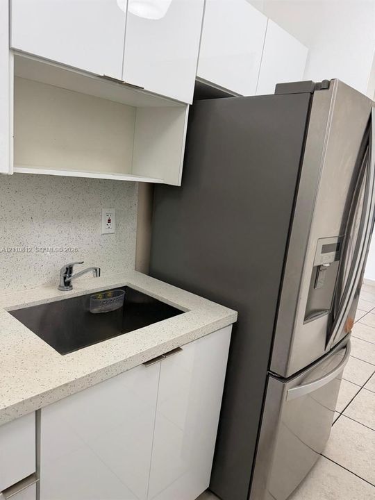 Kitchen area featuring high-gloss white cabinetry, speckled stone-finish countertops, an undermount sink with a chrome-finish faucet, and a stainless steel French-door refrigerator