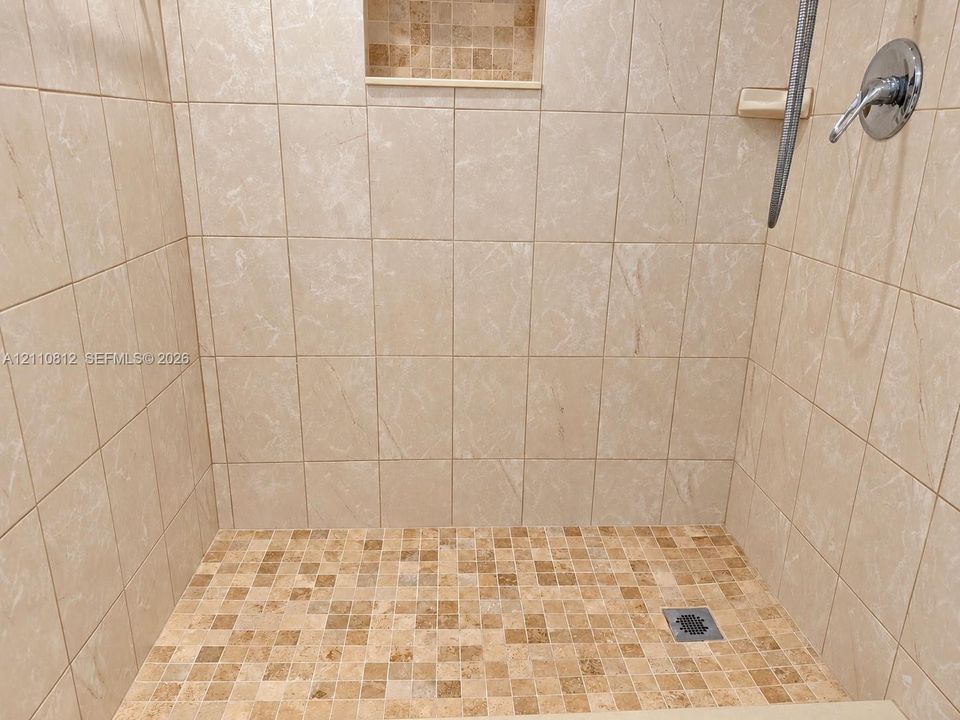 Shower stall featuring large-format ceramic wall tile, mosaic tile flooring, a built-in recessed niche, and a single-handle wall-mounted shower fixture