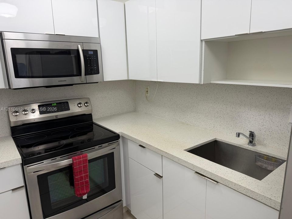 Kitchen featuring high-gloss white cabinetry, speckled composite countertops, stainless steel appliances, and an undermount rectangular sink