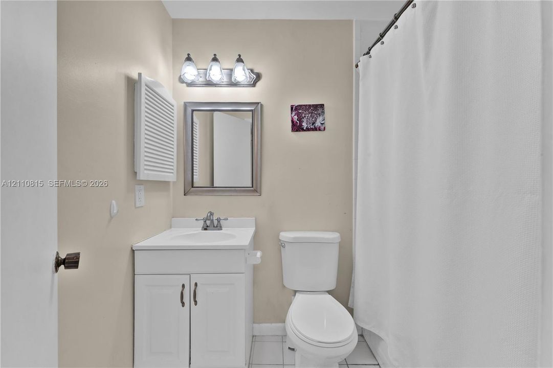Bathroom featuring a white vanity cabinet with a stone-top integrated sink, a framed wall mirror, a three-light vanity fixture, and tiled flooring