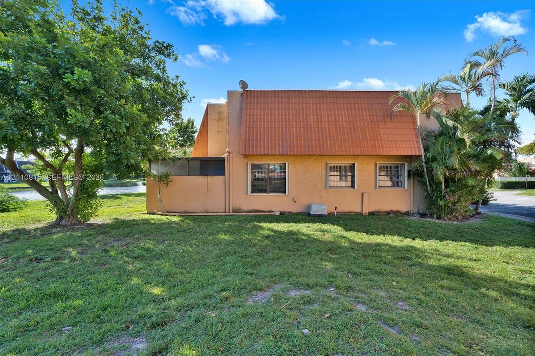Stucco exterior featuring a dual-pitch clay tile roof, horizontal sliding windows, and an expansive lawn with mature trees