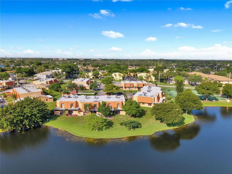 Aerial perspective featuring waterfront grounds, mature trees, expansive manicured lawn, and on-site recreational court