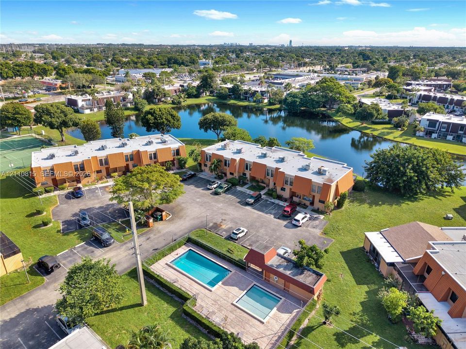 Aerial perspective of multi-unit residential buildings featuring a community swimming pool, paved surface parking, and waterfront grounds