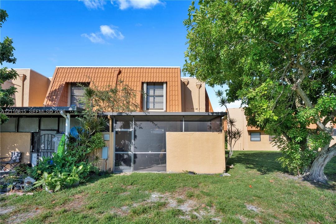 Stucco exterior featuring a metal mansard roof, screened-in lanai, and mature landscaping