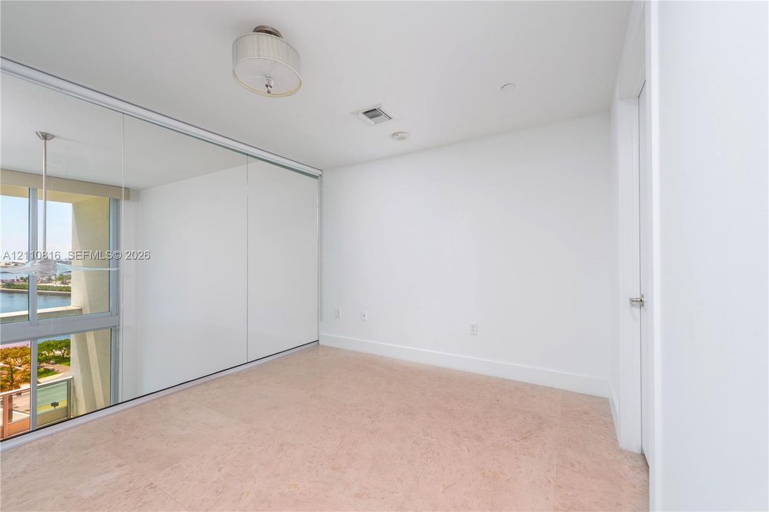 Floor-to-ceiling sliding glass doors, full-length wall mirror, neutral stone flooring, flush-mount drum light fixture, and floor-to-ceiling windows