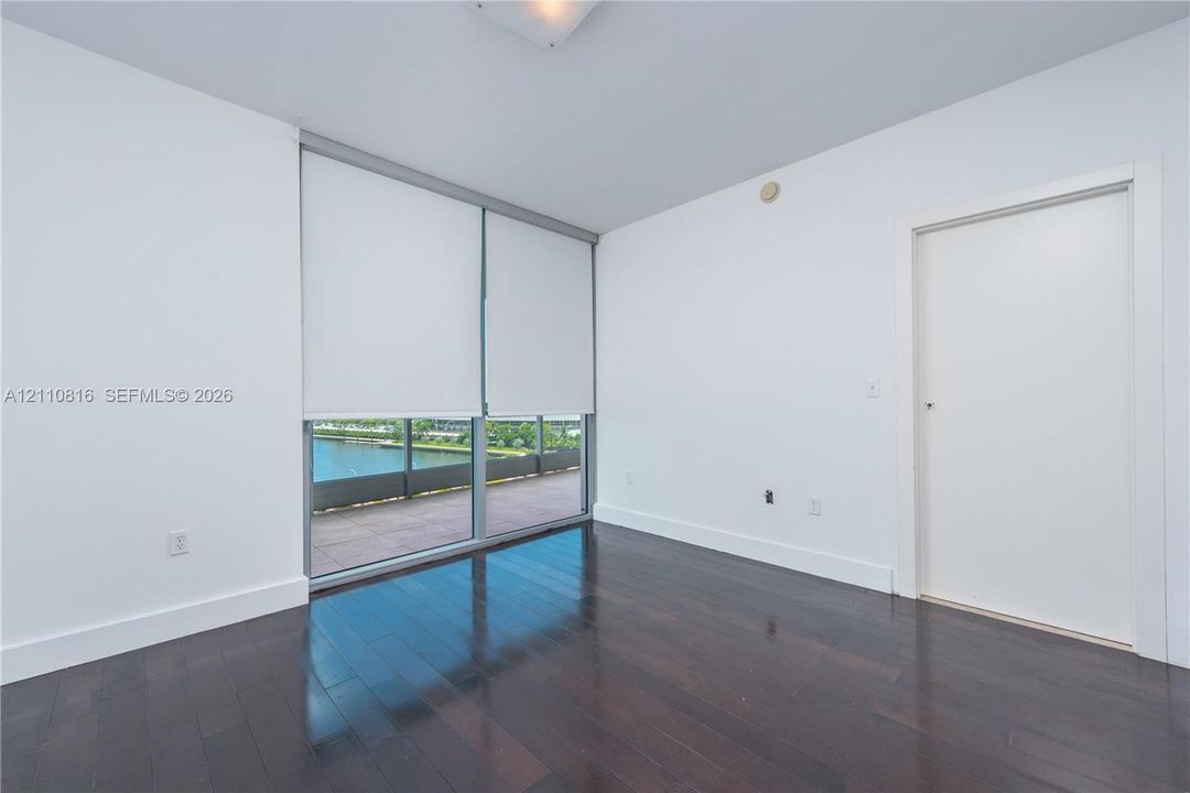 Room featuring dark wood-finish flooring, floor-to-ceiling windows, and access to a balcony with water scenery
