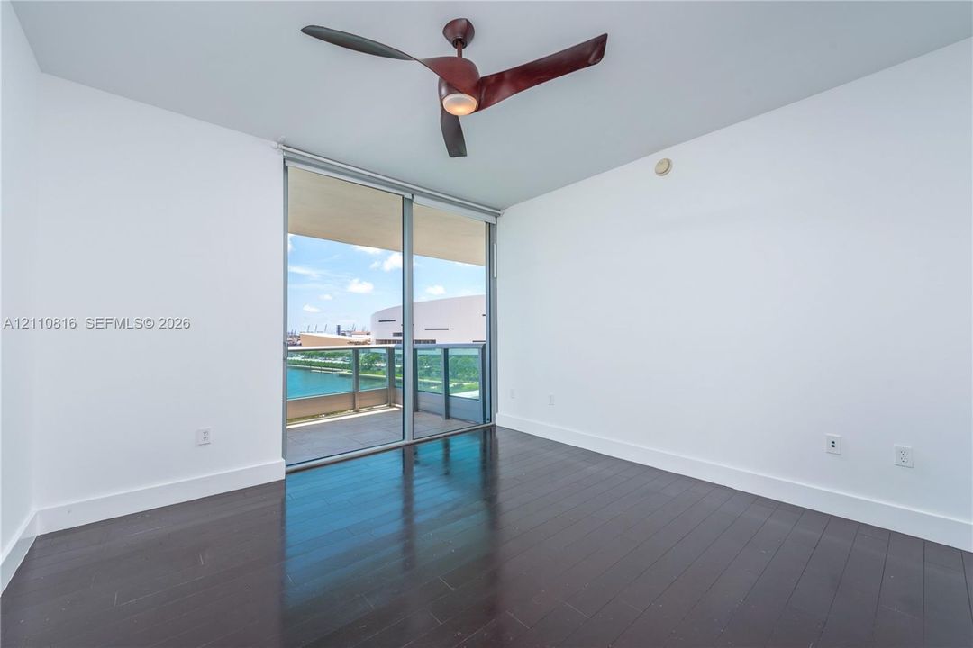 Dark wood-finish flooring, floor-to-ceiling glass sliding door, private balcony, and three-blade ceiling fan with integrated lighting