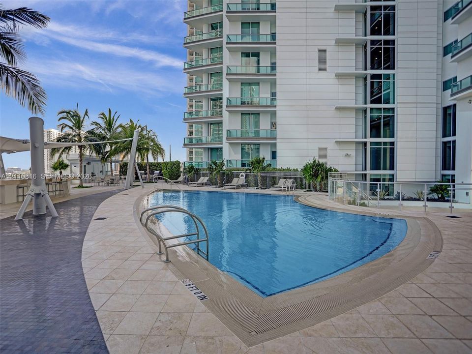 Swimming pool featuring a stone-tile deck, integrated metal handrails, and a built-in shade structure