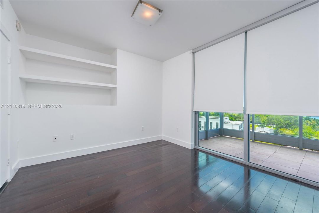 Interior space featuring dark wood-finish flooring, built-in recessed shelving, floor-to-ceiling glass sliding doors, and an attached balcony with tile flooring