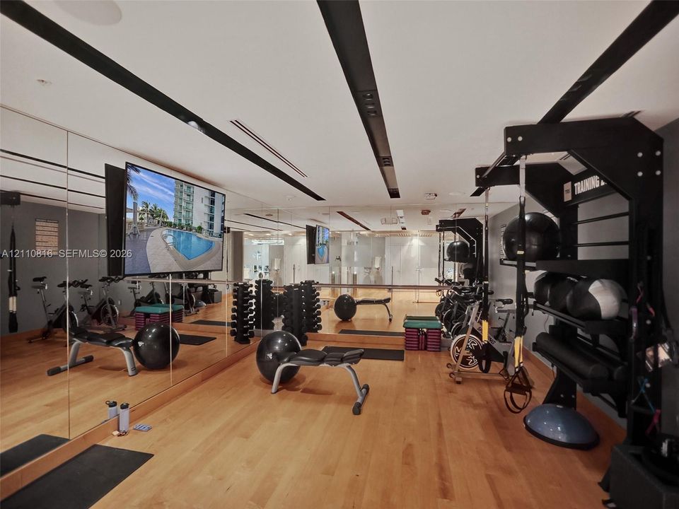 Fitness space featuring wood-finish flooring, extensive floor-to-ceiling mirrored walls, and recessed ceiling lighting
