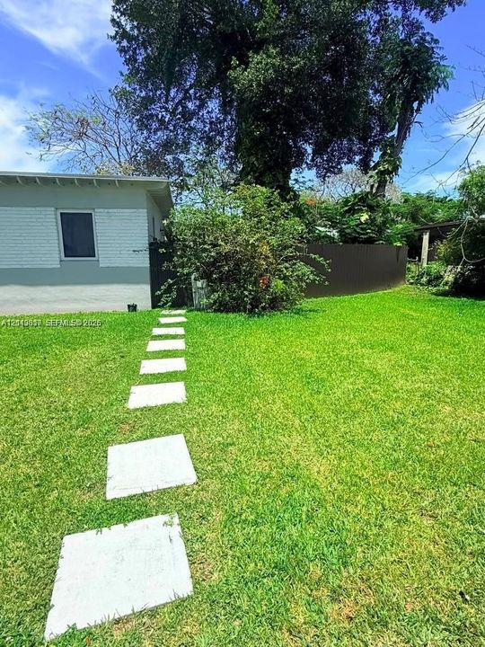 Expansive backyard featuring a manicured lawn, stone paver pathway, privacy fencing, and mature trees