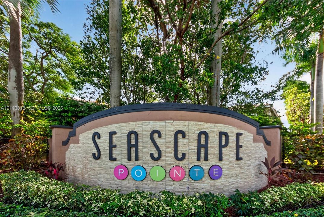 Community signage featuring stone-finish masonry, elevated trim detailing, and established landscaping with mature trees