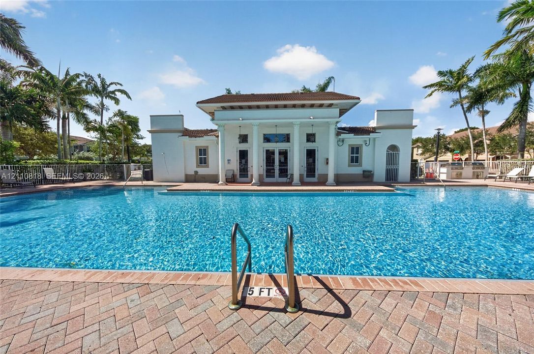 In-ground swimming pool with brick paver decking, classical architectural columns, and surrounding palm trees