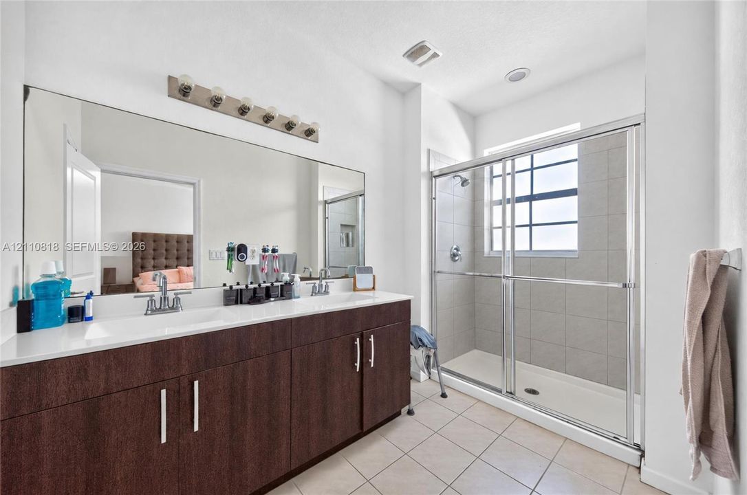 Double vanity with dark wood-finish cabinetry, solid surface countertop, and dual integrated sinks, paired with a glass-enclosed shower featuring tile surround and natural lighting