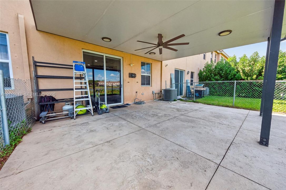 Covered concrete patio featuring a ceiling fan and recessed lighting, sliding glass door access, and a chain-link fenced yard