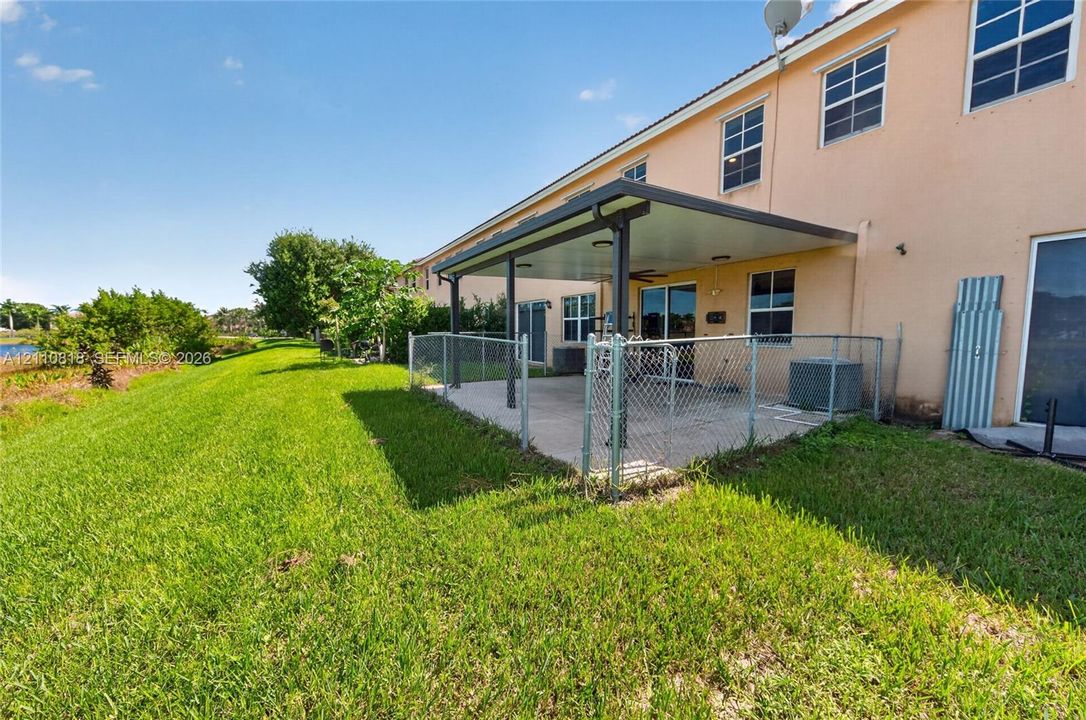 Rear exterior featuring a covered concrete patio, chain-link fencing, stucco siding, and multi-pane windows