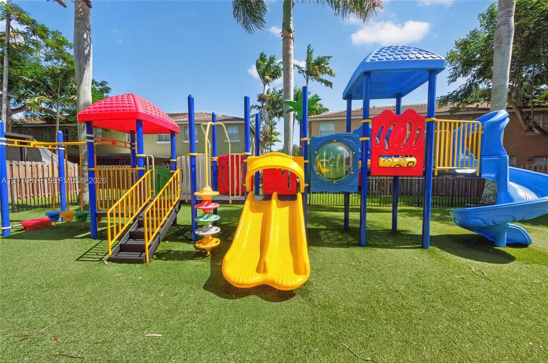 Outdoor recreation area featuring a multi-component play structure with dual slides, a spiral slide, and synthetic turf ground cover