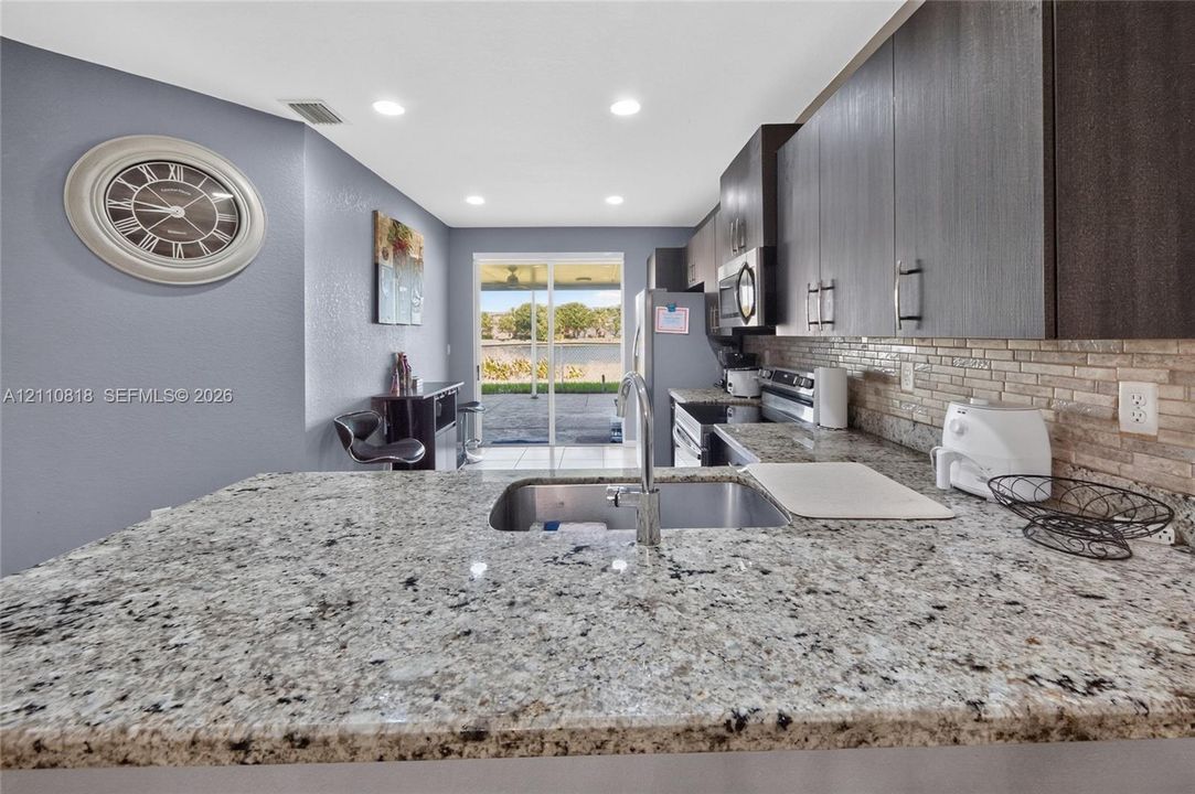 Kitchen featuring stone countertops, undermount stainless steel sink, tile backsplash, dark wood cabinetry, and recessed lighting