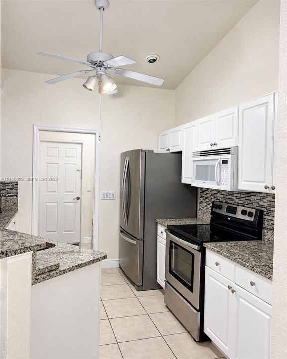 Kitchen featuring white cabinetry, stone-surface countertops, mosaic tile backsplash, stainless steel appliances, and tile flooring
