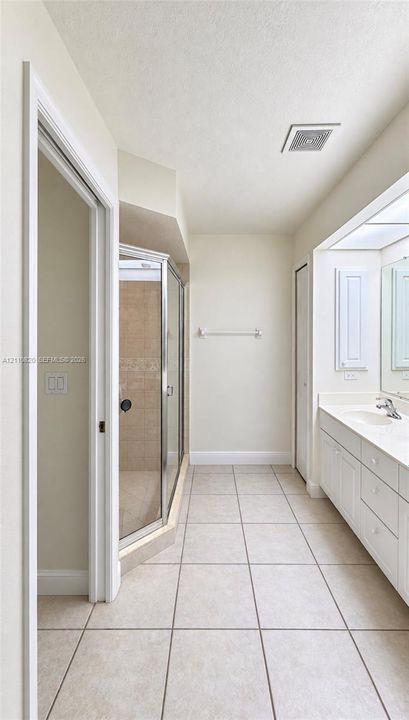 Bathroom featuring a large vanity with integrated countertop, tiled flooring, corner glass-enclosed shower, and built-in cabinetry