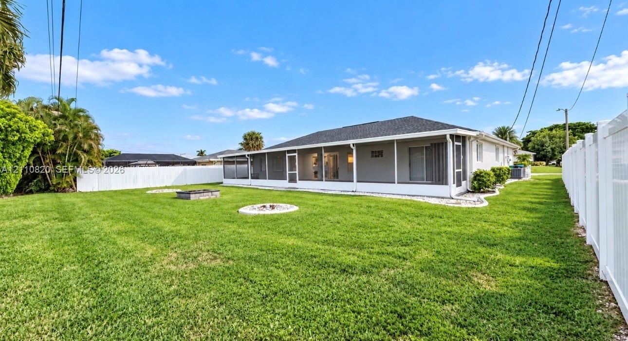 Expansive backyard featuring a screened-in lanai, stone-bordered fire pit area, and white vinyl perimeter fencing