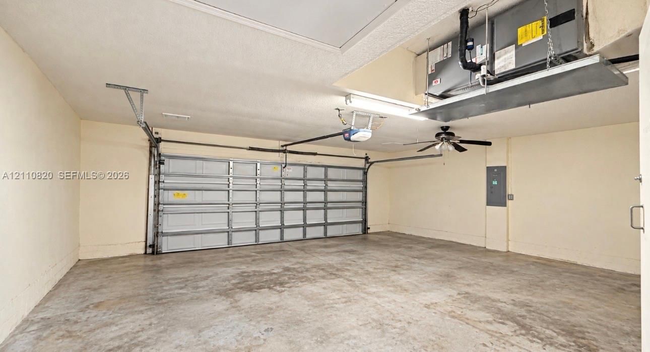 Attached garage featuring a sectional roll-up door, ceiling-mounted fan, overhead lighting, and an integrated air handling unit