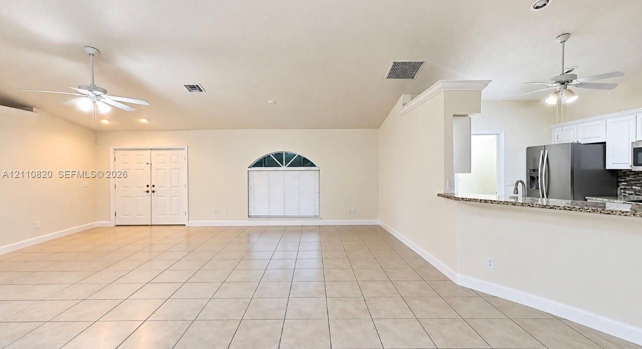 Open-concept interior featuring light-toned tile flooring, dual ceiling fans, a vaulted ceiling, arched window, and a kitchen breakfast bar with stone-finish countertops