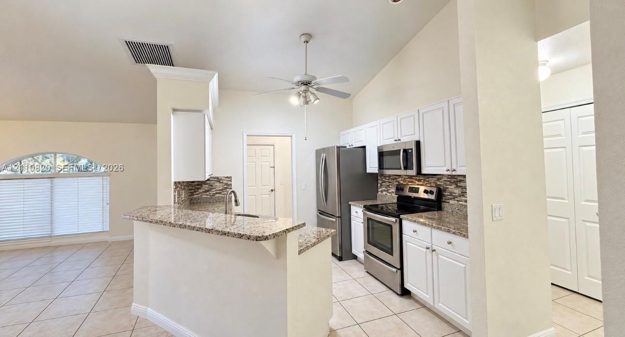 Kitchen featuring white cabinetry, stone-finish countertops, stainless steel appliances, tile flooring, and vaulted ceilings