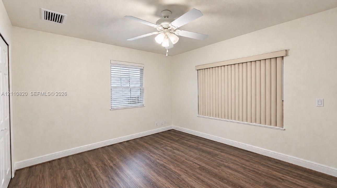 Wood-finish flooring, white ceiling fan with integrated light fixture, and windows equipped with neutral vertical and horizontal blinds