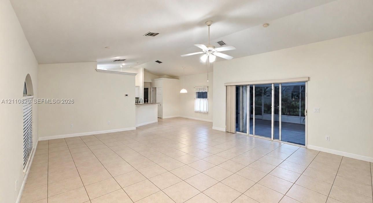 Open-concept interior featuring vaulted ceilings, neutral ceramic tile flooring, a ceiling fan with integrated lighting, and glass sliding doors
