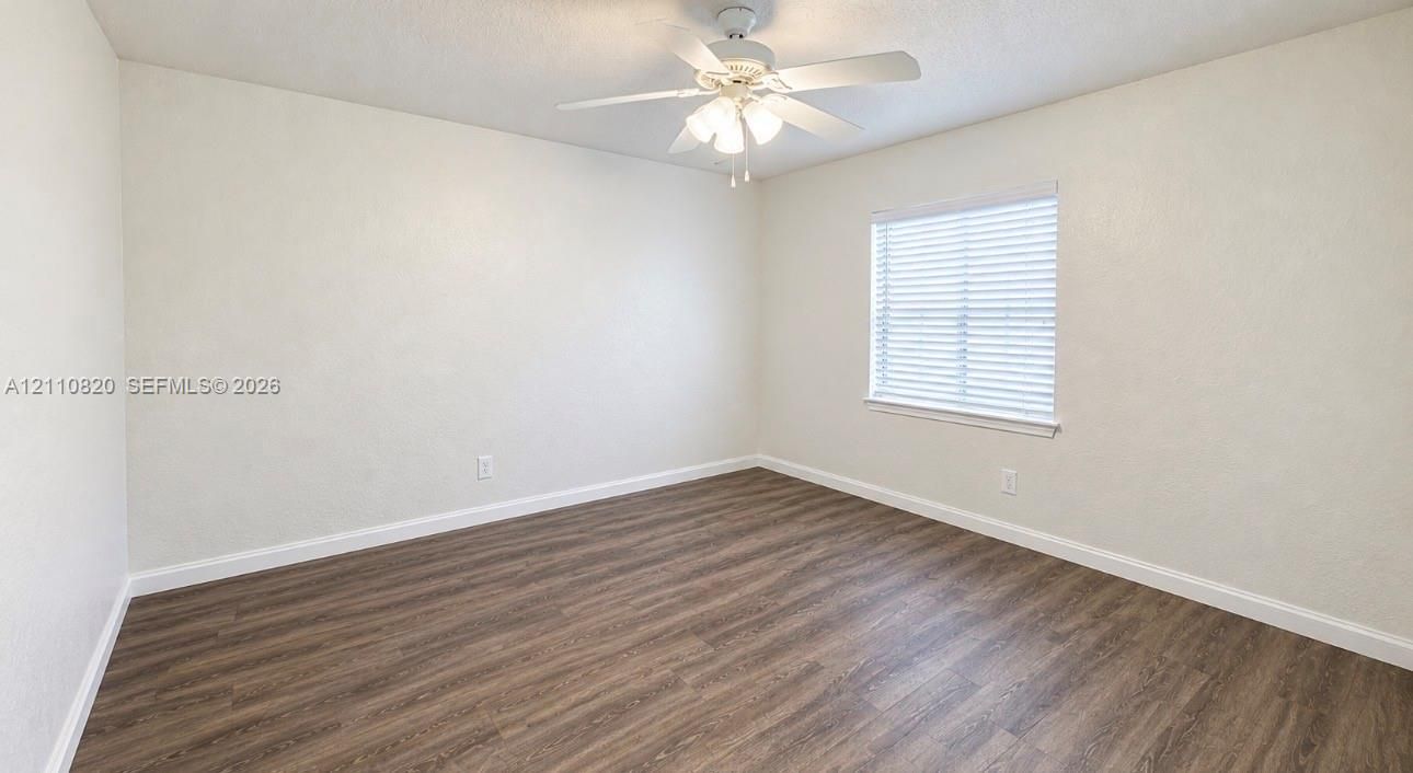 Neutral interior featuring wood-finish flooring, crisp white walls, a multi-light ceiling fan, and a window with horizontal blinds