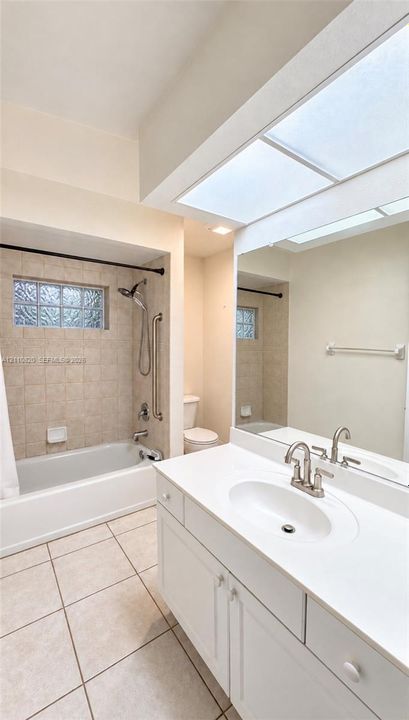 Bathroom featuring a white vanity with an integrated basin, large-format mirror, recessed ceiling lighting, tile flooring, and a shower-tub combination with tile surround and glass block window