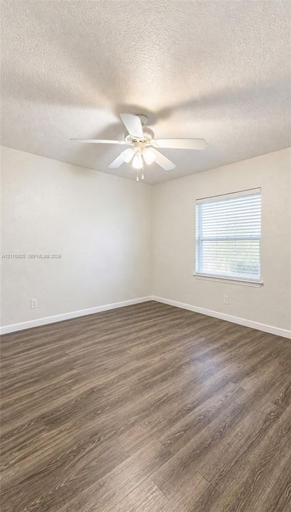 Interior space featuring wood-finish flooring, a multi-blade ceiling fan with integrated lighting, and a window with horizontal blinds