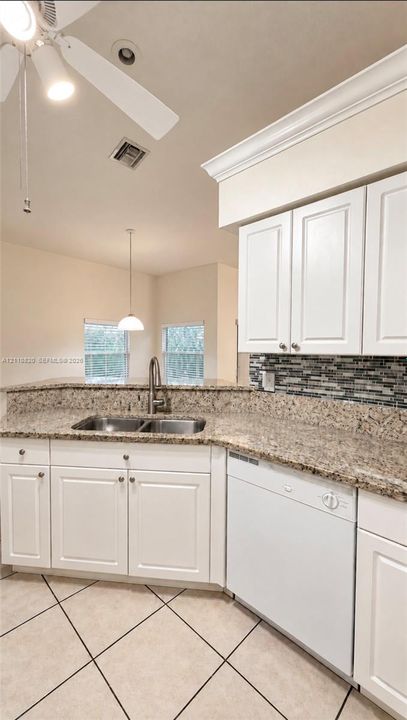 Kitchen featuring white shaker-style cabinetry, stone-surface countertops, mosaic tile backsplash, double-basin stainless steel sink with pull-down faucet, and diagonal-set ceramic tile flooring