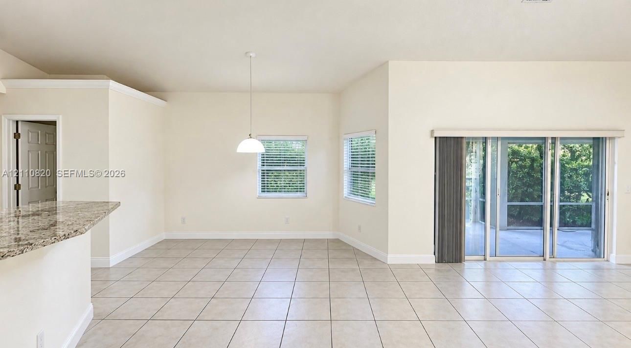 Open-concept interior featuring light-toned tile flooring, granite-surfaced breakfast bar, pendant lighting, and sliding glass doors with access to an exterior screen enclosure