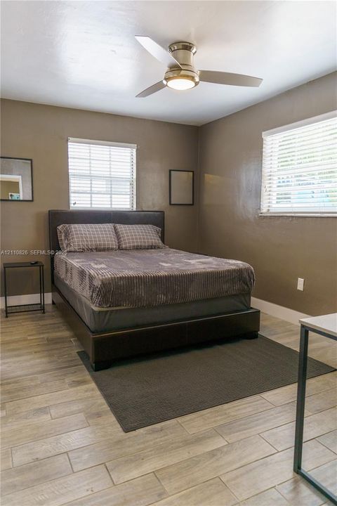 Wood-finish tile flooring, dual windows with horizontal blinds, and brushed-nickel ceiling fan with integrated lighting