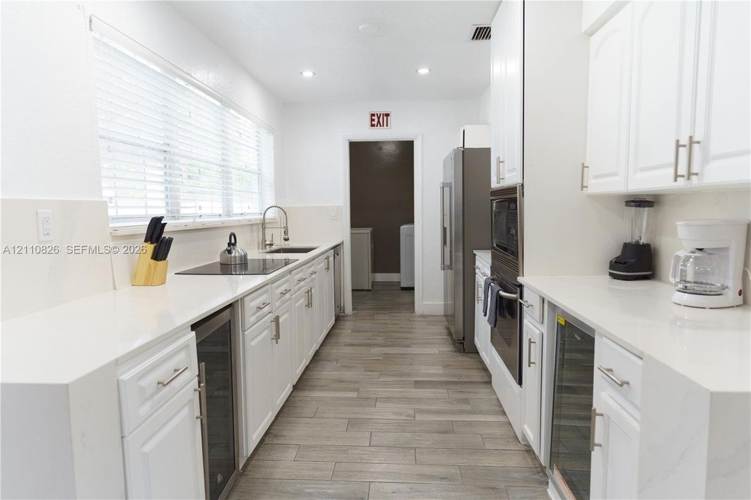 Kitchen featuring white cabinetry, solid-surface countertops, wood-finish tile flooring, a built-in double oven, and stainless steel integrated wine refrigerators