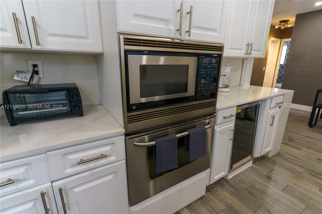Kitchen featuring white Shaker-style cabinetry, quartz countertops, a built-in stainless steel microwave and oven combination, a stainless steel under-counter beverage cooler, and wood-finish flooring
