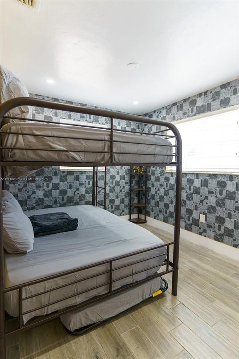 Room featuring wood-finish flooring, patterned wallpaper, and horizontal blinds