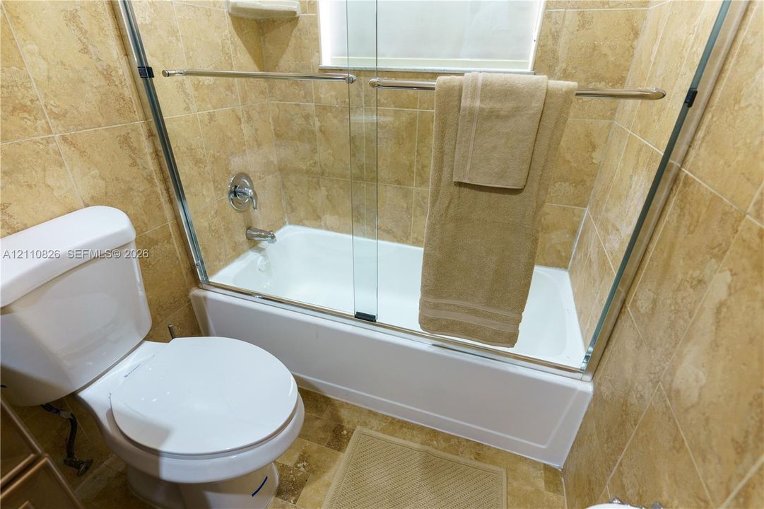 Bathtub with a glass sliding enclosure, floor-to-ceiling tile surround, and built-in ceramic soap dish