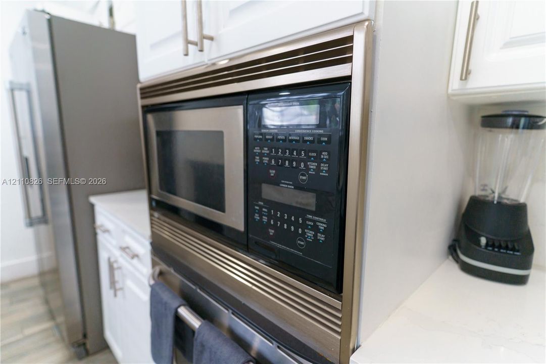 Built-in stainless steel microwave oven, white cabinetry featuring brushed metal hardware, and solid-surface countertops