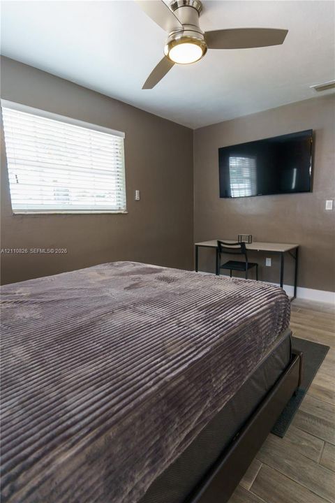 Interior space featuring wood-finish flooring, neutral wall tones, a ceiling fan with integrated light fixture, and horizontal window blinds
