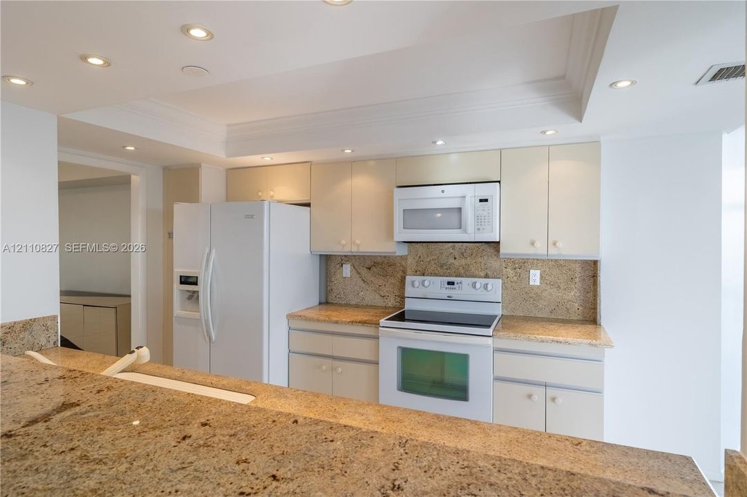 Kitchen featuring stone countertops, integrated cabinetry, white appliances, and recessed ceiling lighting