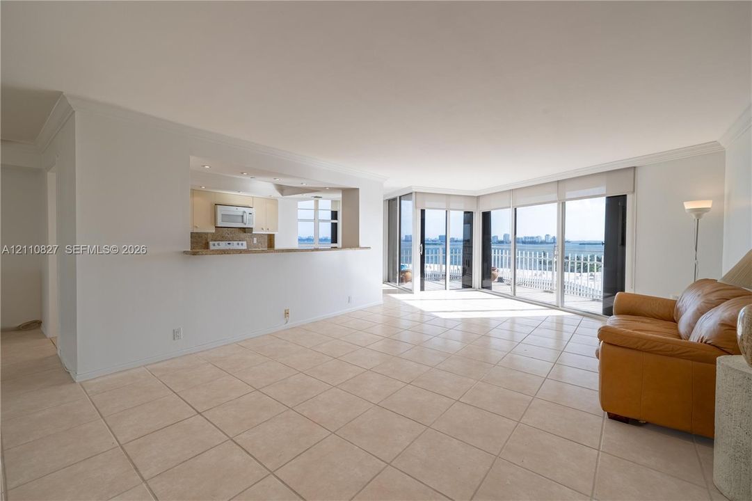 Open-concept area featuring light-toned ceramic tile flooring, a pass-through kitchen counter, and floor-to-ceiling glass sliding doors leading to an exterior balcony