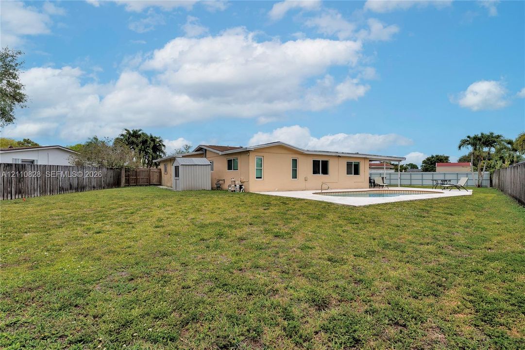 Expansive backyard featuring a concrete patio, in-ground swimming pool, storage shed, and perimeter wood fencing